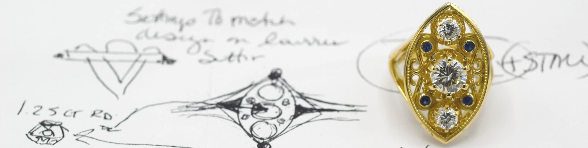 Image of custom ring design process- actual ring sitting on a paper with various sketches from earlier in the process. 
