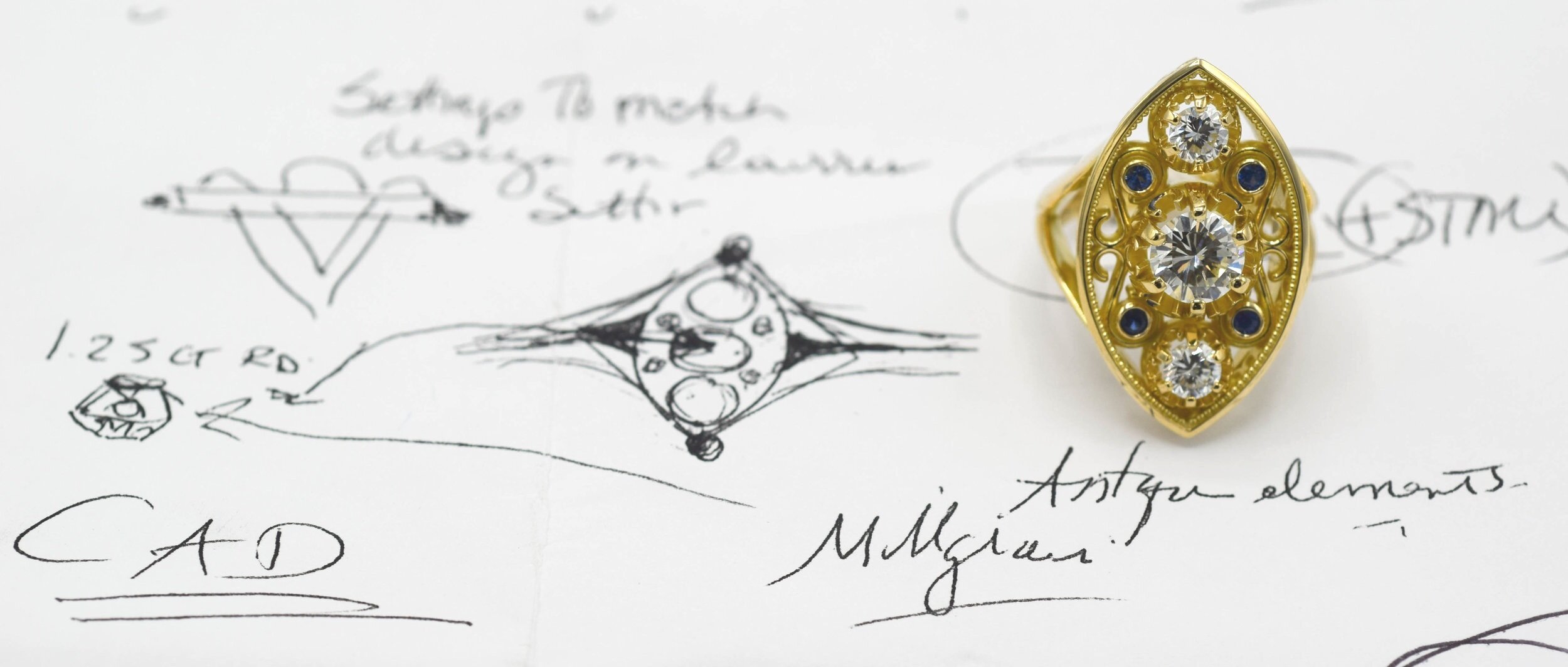 Image of custom ring design process- actual ring sitting on a paper with various sketches from earlier in the process. 