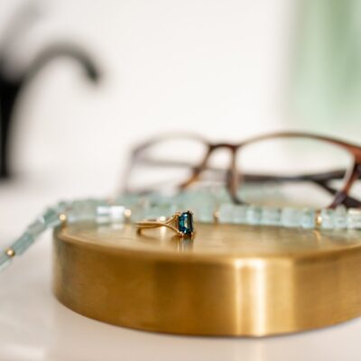 Ring, necklace, and glasses, in front of a blurred sink faucet