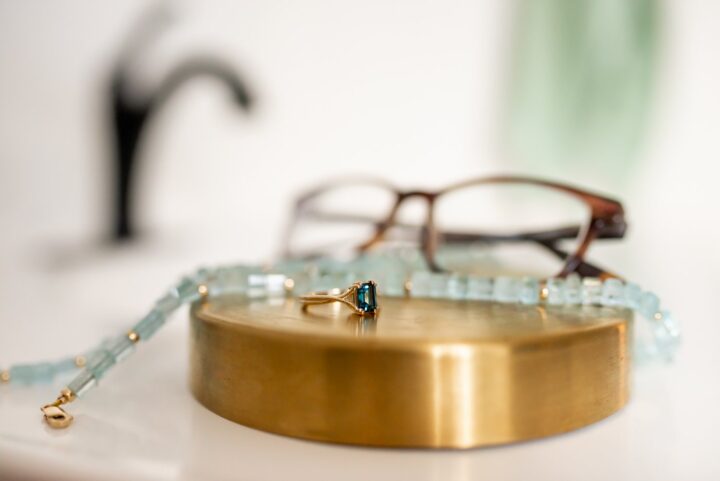Ring, necklace, and glasses, in front of a blurred sink faucet